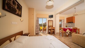 A hotel room with a bed, a dining table, chairs, a kitchen area, and a balcony with a view. - Lorenzo House Apartments (Kefalonia)