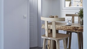 Eine moderne Küche mit einem rustikalen Holztisch und Hockern, weißen Wänden und einer durch ein Fenster sichtbaren Steinwand.