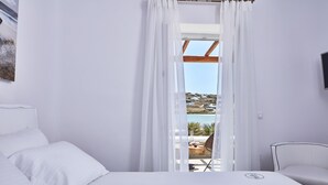 Ein Zimmer mit einem Bett, einem Sessel und Blick auf einen Pool sowie umliegende Gebäude.
