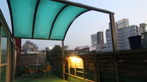 An outdoor seating area with a table and chairs, a green awning, and a view of city buildings in the background. - Hotel FA (Seoul)