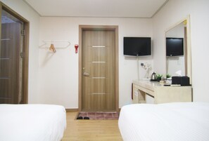 A hotel room with two beds, a wooden door, a television mounted on the wall, and a small desk with a mirror and a plant. - Hotel FA (Seoul)