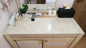 A hotel room with a marble countertop, a small refrigerator, a mirror, a plant, a telephone, a remote control, and a tissue box. - Hotel FA (Seoul)