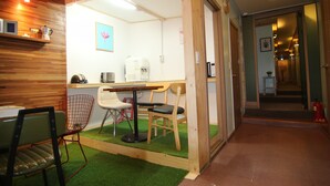 A small, cozy room with a wooden ceiling, a green artificial grass floor, a table with chairs, a coffee machine, and a shelf with items. - Hotel FA (Seoul)