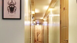 A narrow, carpeted hallway with wooden doors on one side and a framed insect illustration on the wall. - Hotel FA (Seoul)