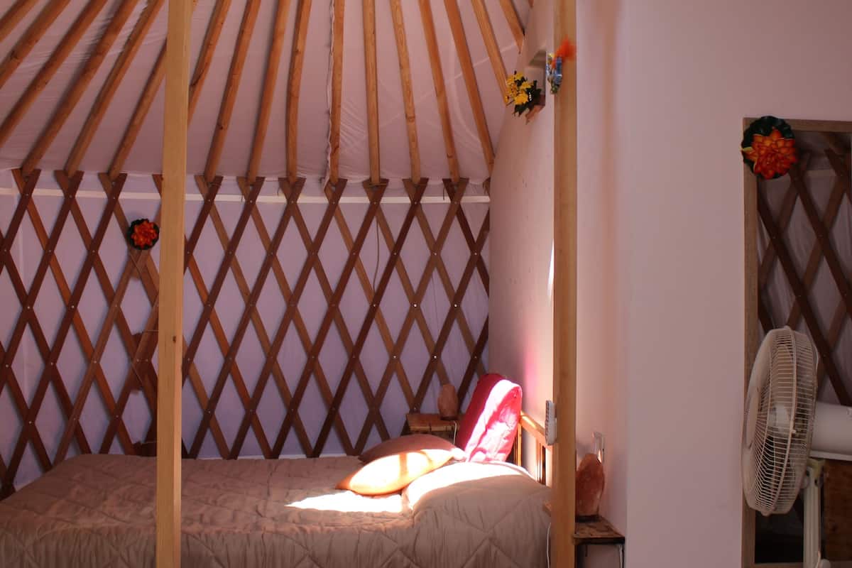 Ein yurtähnliches Zimmer mit einem Bett, Holzlattengittern, einem Ventilator und einem Fenster.