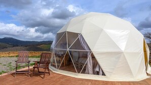 A geodesic dome tent with a clear interior, two wooden chairs outside, and a view of hills in the background. - Azienda Agricola Pietra Serena B&B (Civitella Paganico)