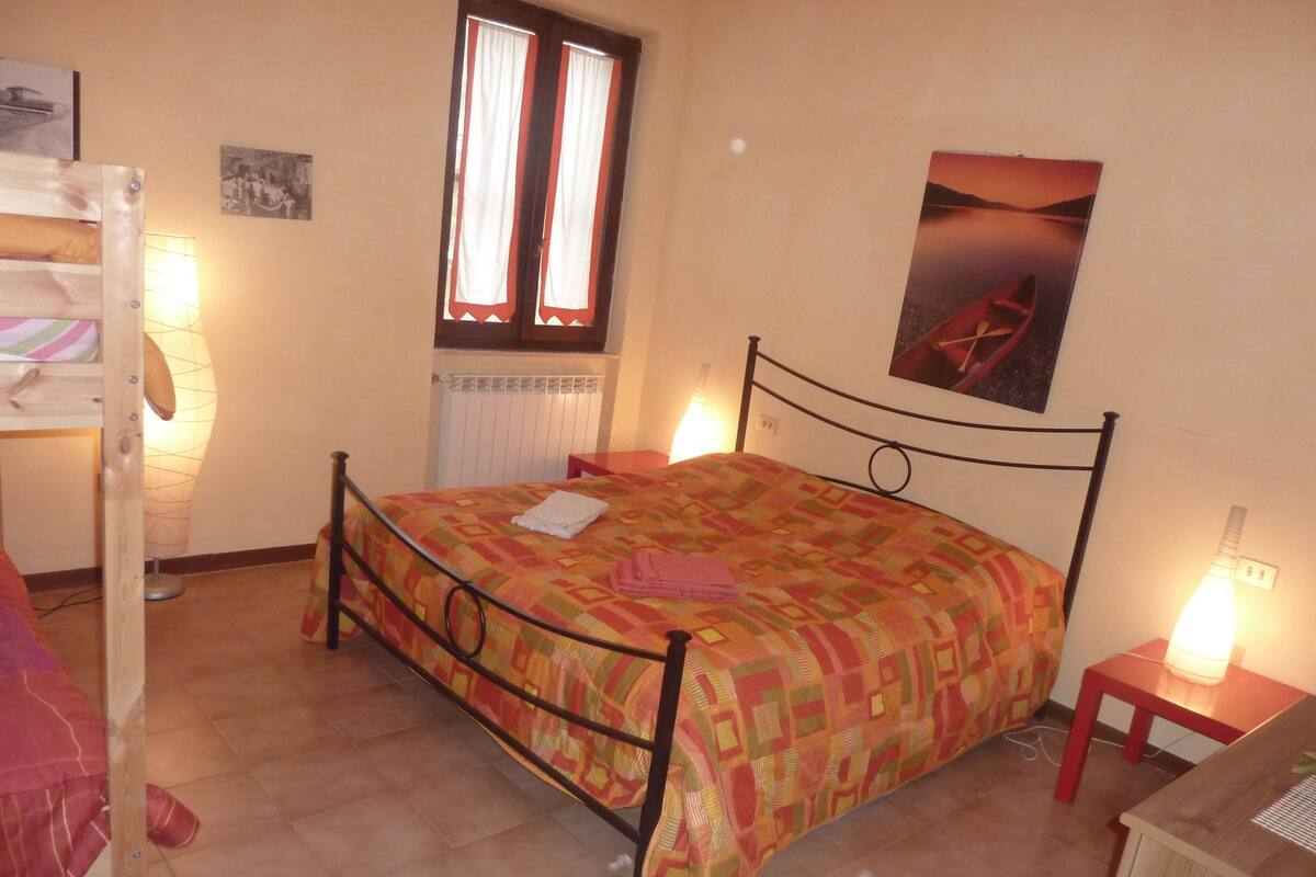 Ein Schlafzimmer mit Bett, einem fensterbündigen Vorhang, einem Wandbild und einem Nachttisch mit Lampe.