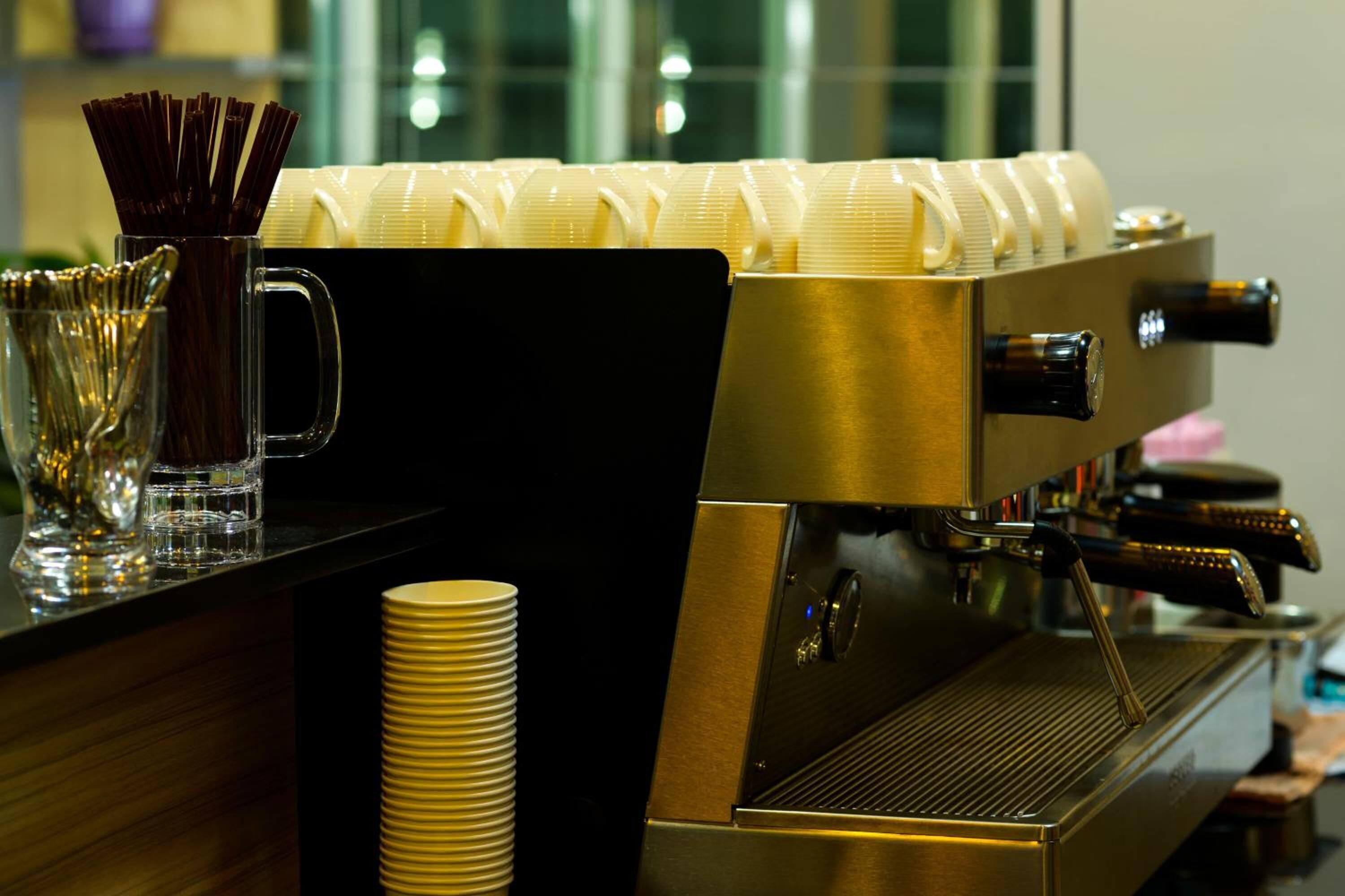 A coffee machine with a milk frother and a stack of disposable cups.