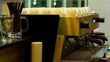 A coffee machine with a milk frother and a stack of disposable cups.