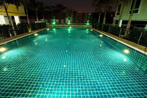 A swimming pool with a grid pattern, surrounded by a low fence and palm trees.