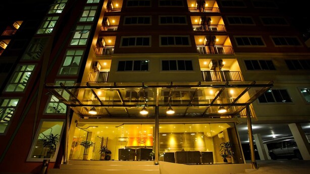 A multi-story hotel with a glass entrance, outdoor seating area, and multiple balconies. - Patt Serviced Apartments (Chonburi)