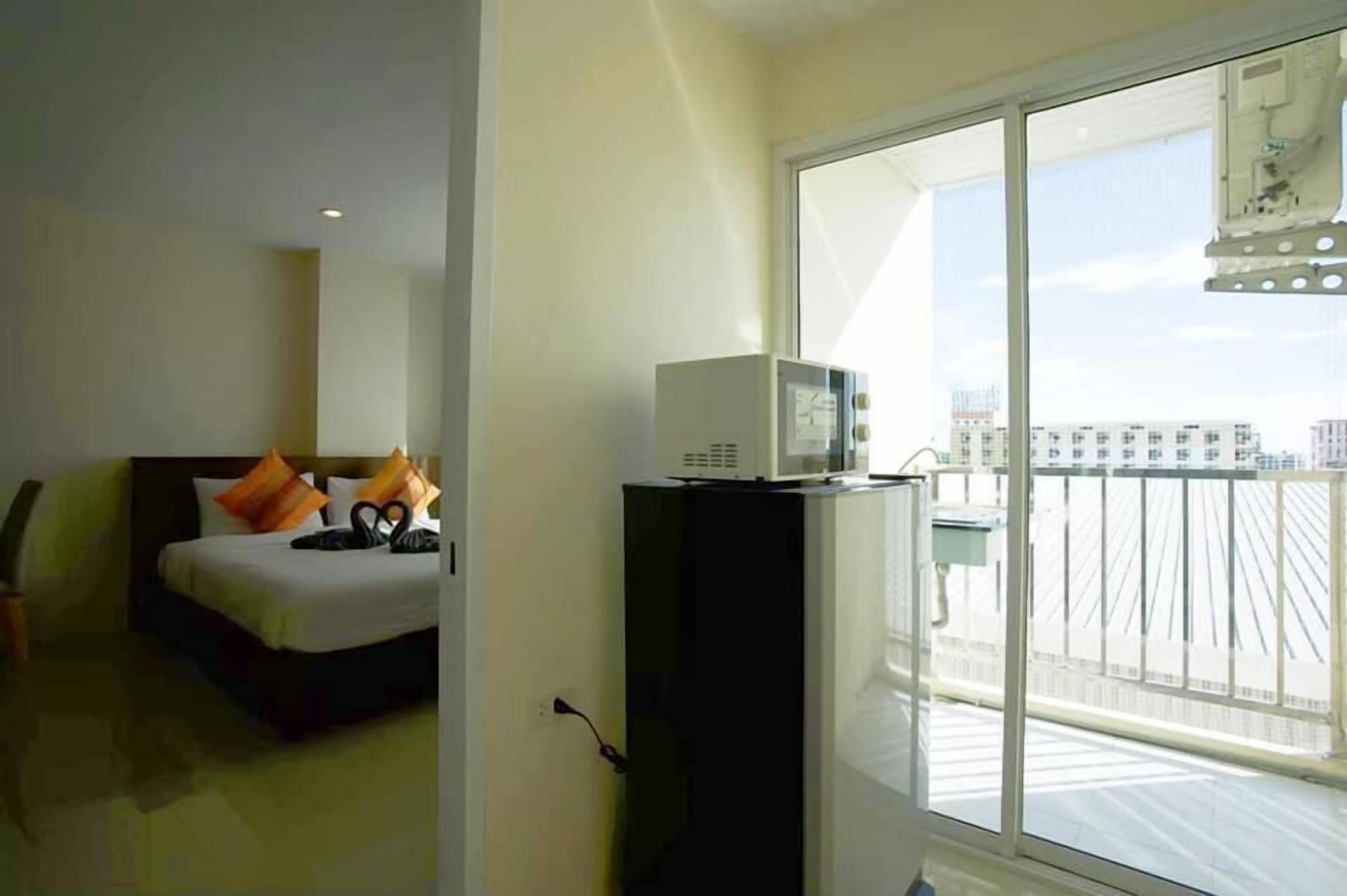 Une chambre d’hôtel avec un lit, un petit bureau équipé d’un micro-ondes et un balcon offrant une vue sur les bâtiments.
