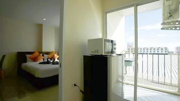 Habitación de hotel con cama, un escritorio pequeño con microondas y balcón con vista a edificios.