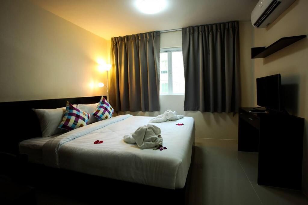 A hotel room with a bed, a bedside table, a television, and a window with curtains.