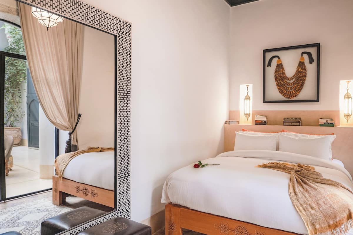 A bedroom with a large bed, a mirror, a wall-mounted artwork, and two wall-mounted lamps.