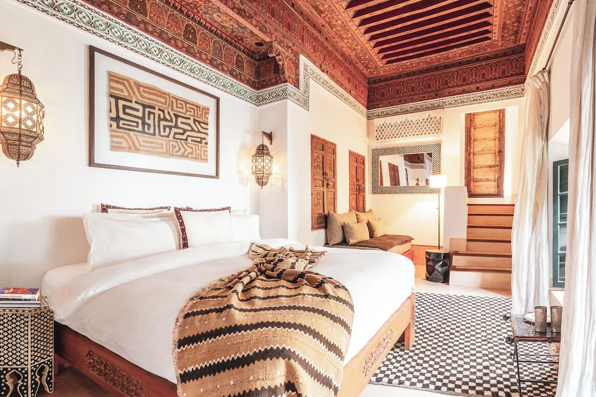 A spacious bedroom with a large bed, a wooden headboard, a patterned throw blanket, and a checkered rug.