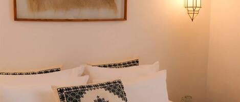A neatly made bed with white linens and decorative pillows, a framed artwork with a star design on the wall, and a wall-mounted light fixture.
