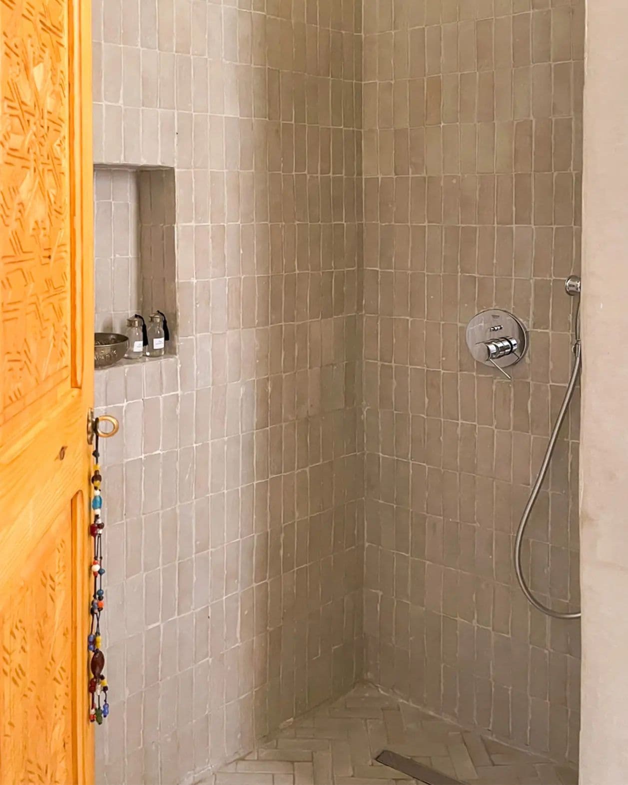 A shower area with tiled walls, a showerhead, and a shelf with bottles.