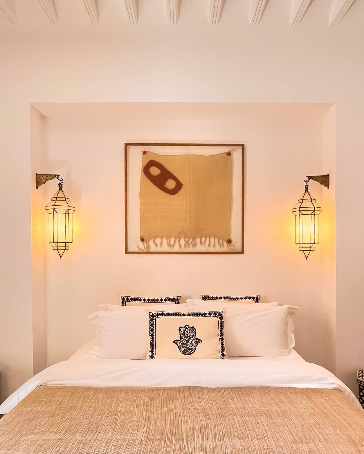 A hotel room with a bed, two wall-mounted lamps, and a framed artwork above the bed.