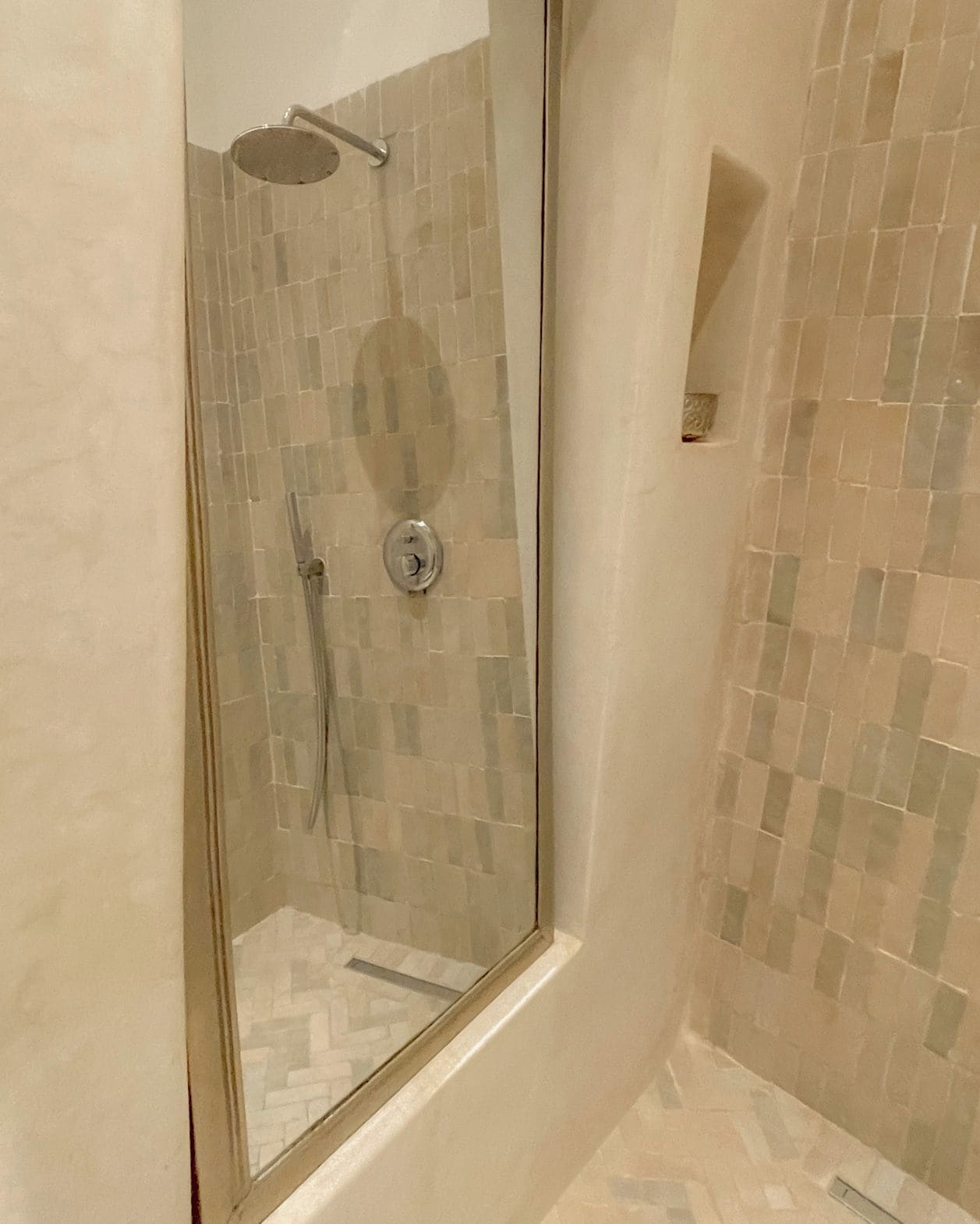 A glass-enclosed shower with a handheld showerhead and a control knob.