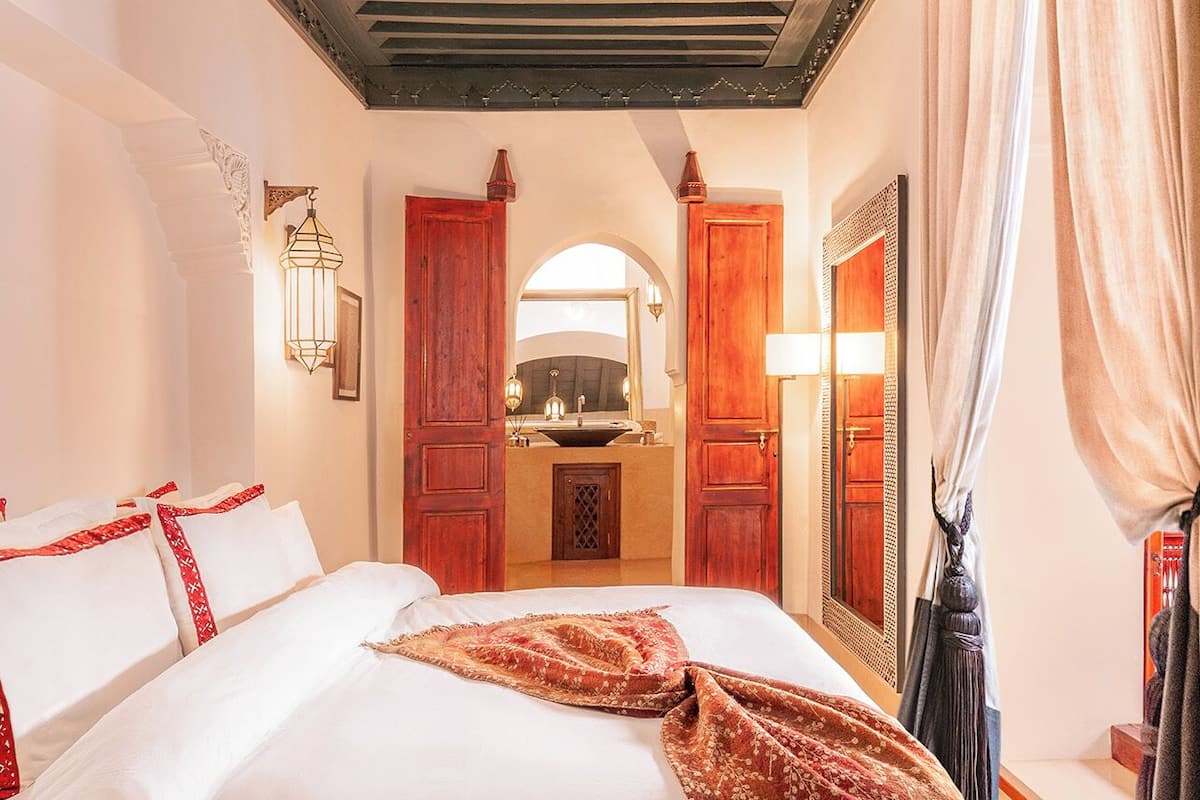 A hotel room with a large bed, a wooden headboard, a mirror, a sink, and a window with curtains.