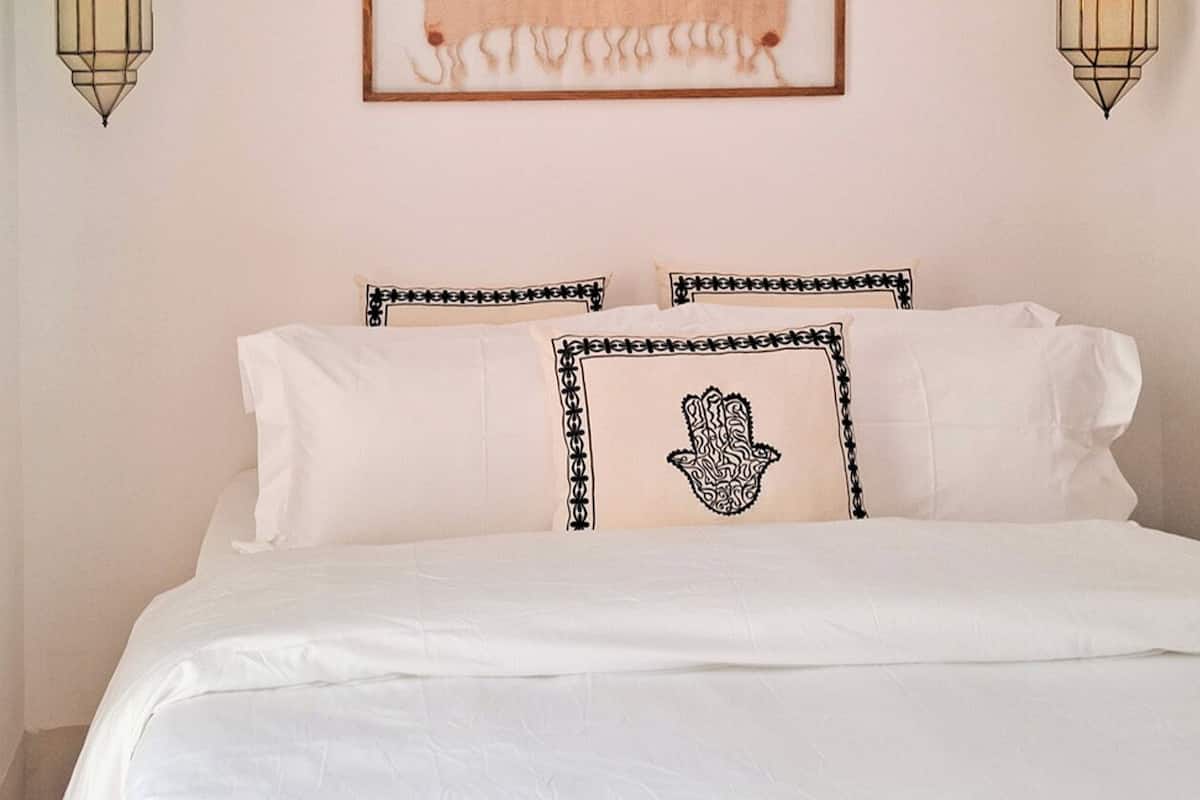 A bed with white linens, a framed tapestry, and two wall-mounted lanterns.