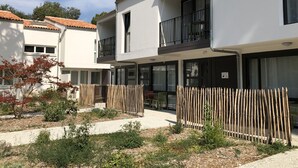 A modern residential building with a balcony, a gated entrance, and a small garden area.