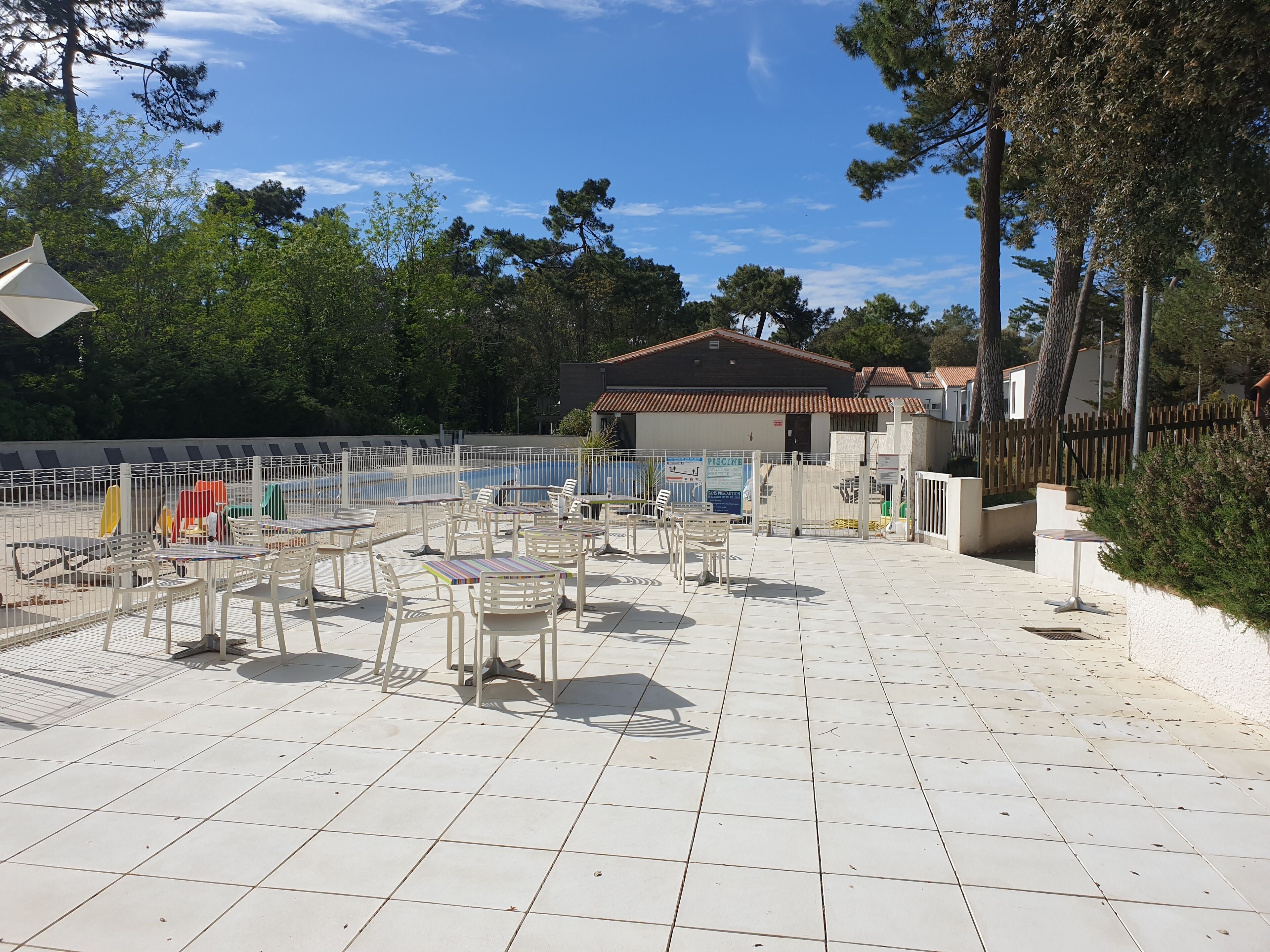 A poolside area with tiled flooring, white outdoor furniture, and a fenced swimming pool.