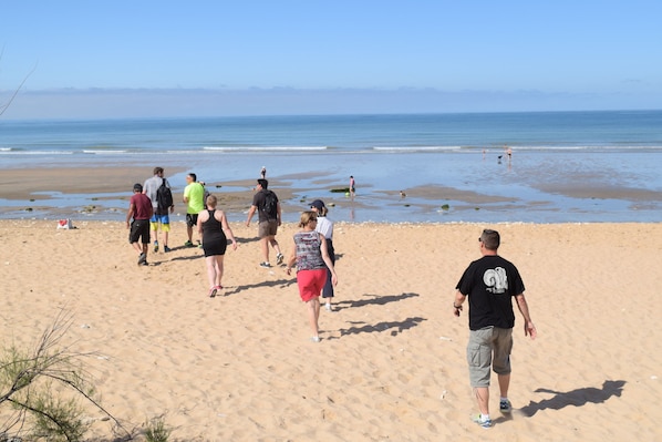 Ein sandiger Strand mit Menschen, die laufen und stehen, und dem Meer im Hintergrund.