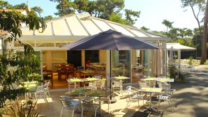 An outdoor cafe with tables and chairs, a large umbrella, and a building with a sloped roof.