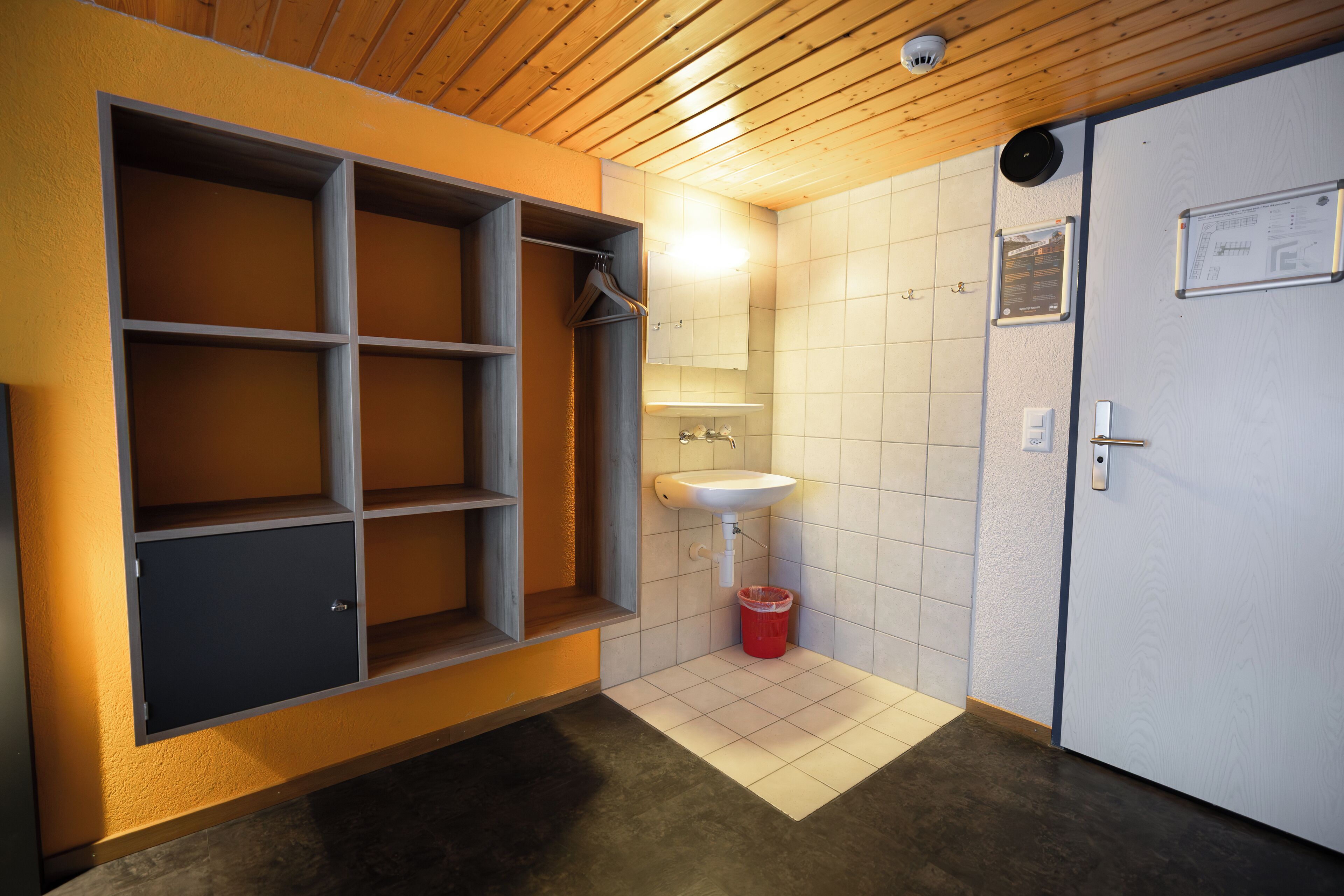 A bathroom with a wooden ceiling, a white sink, a mirror, and a cabinet with shelves.