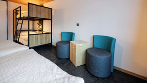 A modern room with a bunk bed, two ottomans, a wooden cabinet, and a lamp. - Eiger Lodge Easy (Grindelwald)