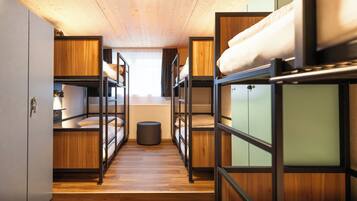A dormitory room with bunk beds, wooden floors, and a small round stool.