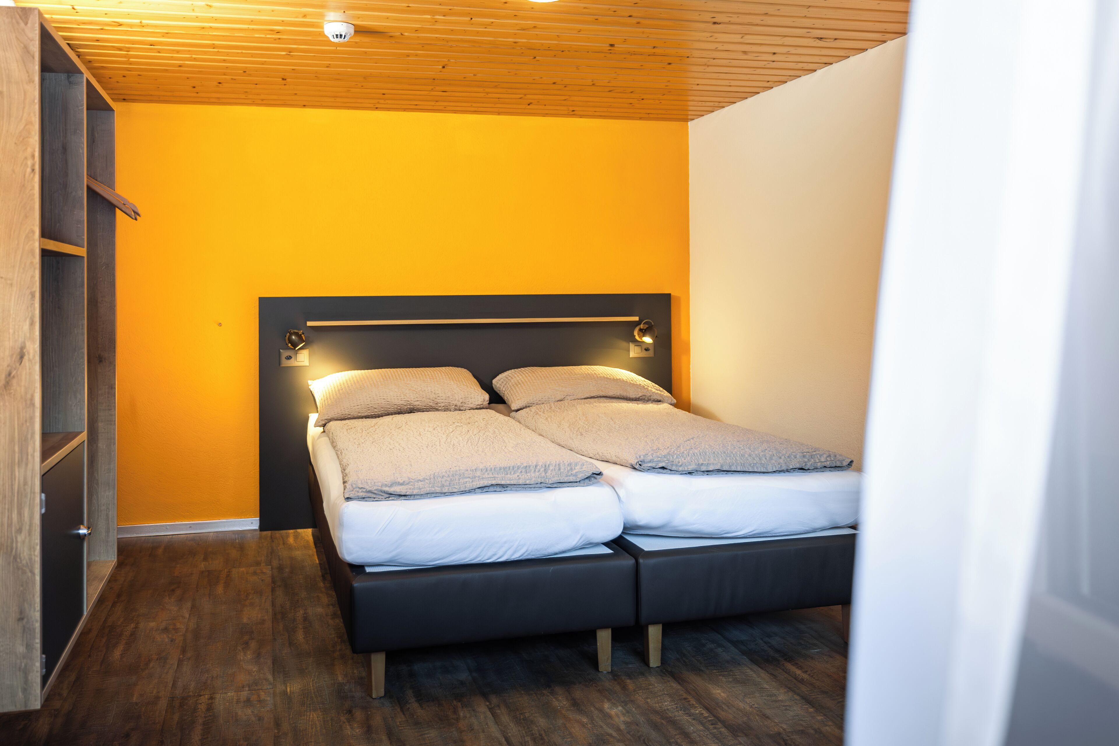 Une chambre à coucher avec un lit, un plancher en bois et un mur jaune.