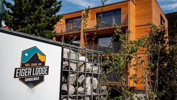 A two-story wooden building with balconies, a sign for 'Eiger Lodge Grindelwald,' and a metal fence.