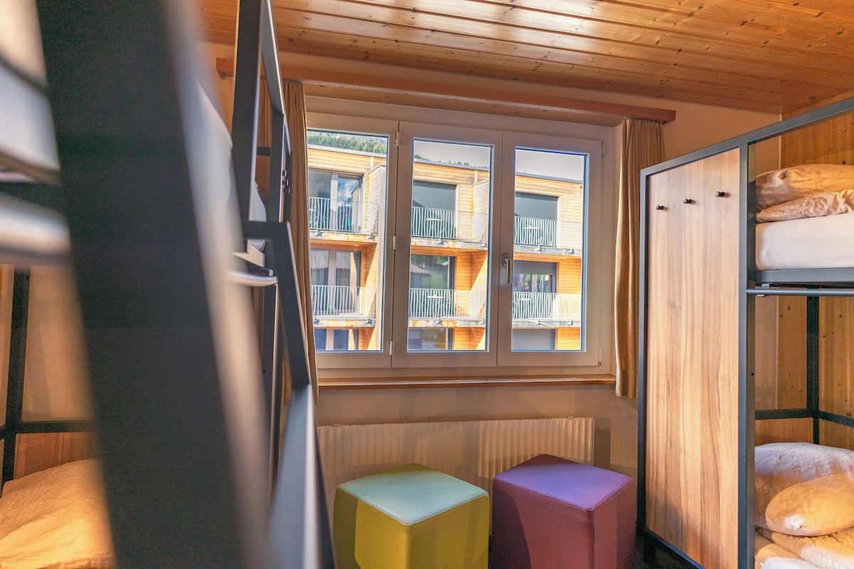 A room with bunk beds, a window with a view of balconies, and a radiator.