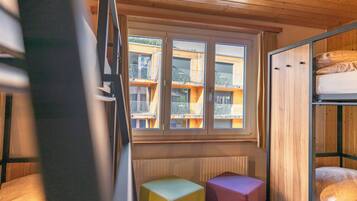 Ein Zimmer mit Etagenbetten, einem Fenster mit Blick auf Balkone und einem Heizkörper.