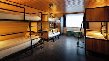 Ein Schlafzimmer mit Etagenbetten, Holzbalkendecke und einem Fenster mit Vorhängen.
