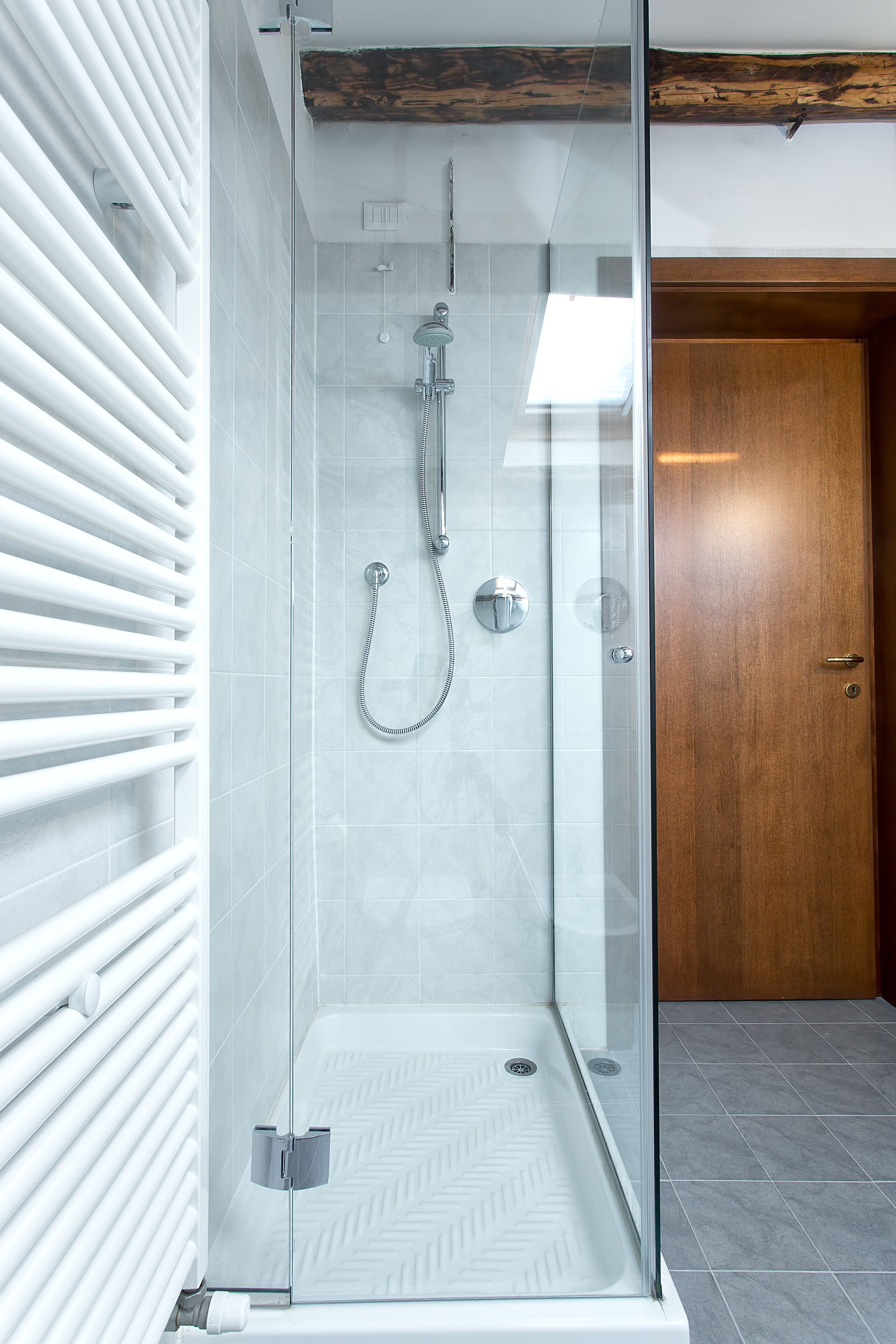 A glass-enclosed shower with a modern design, a wooden door, and a tiled floor.