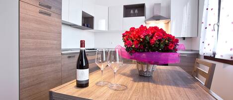 A modern kitchen with wooden cabinets, a dining table with two wine glasses and a bottle, and a vase with red flowers.