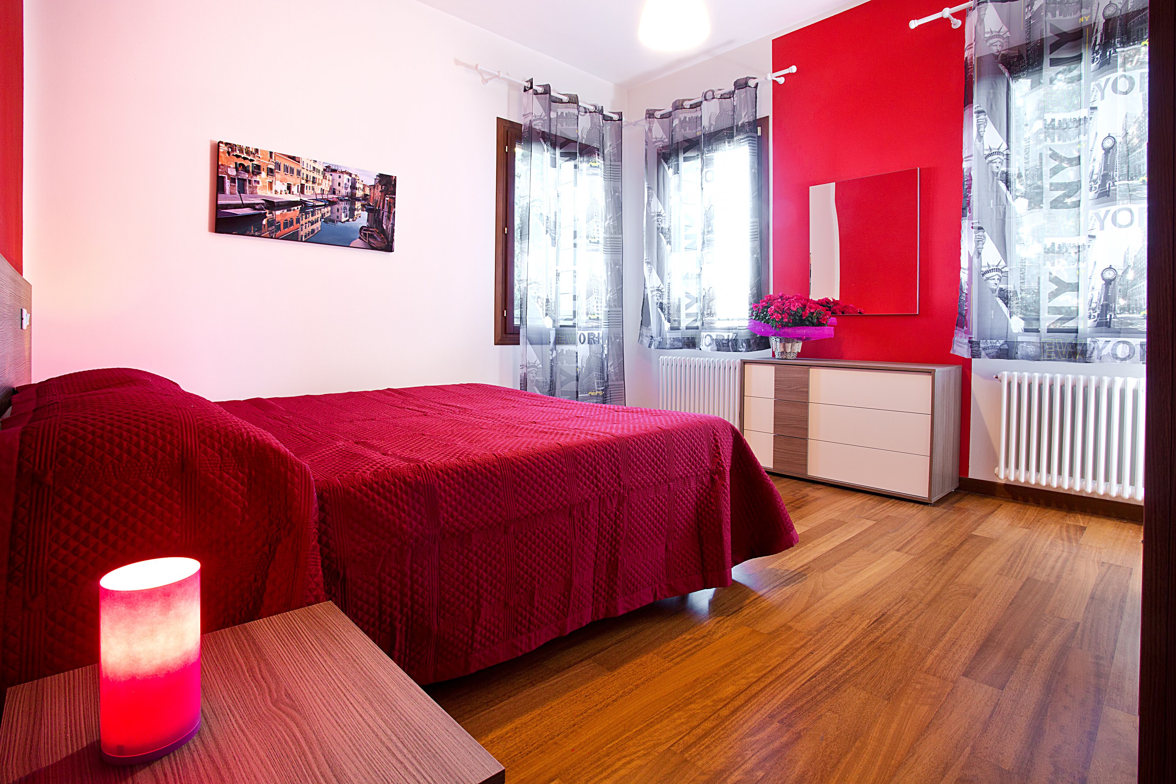 A room with a bed, a bedside table with a lamp, a dresser, and a window with curtains.