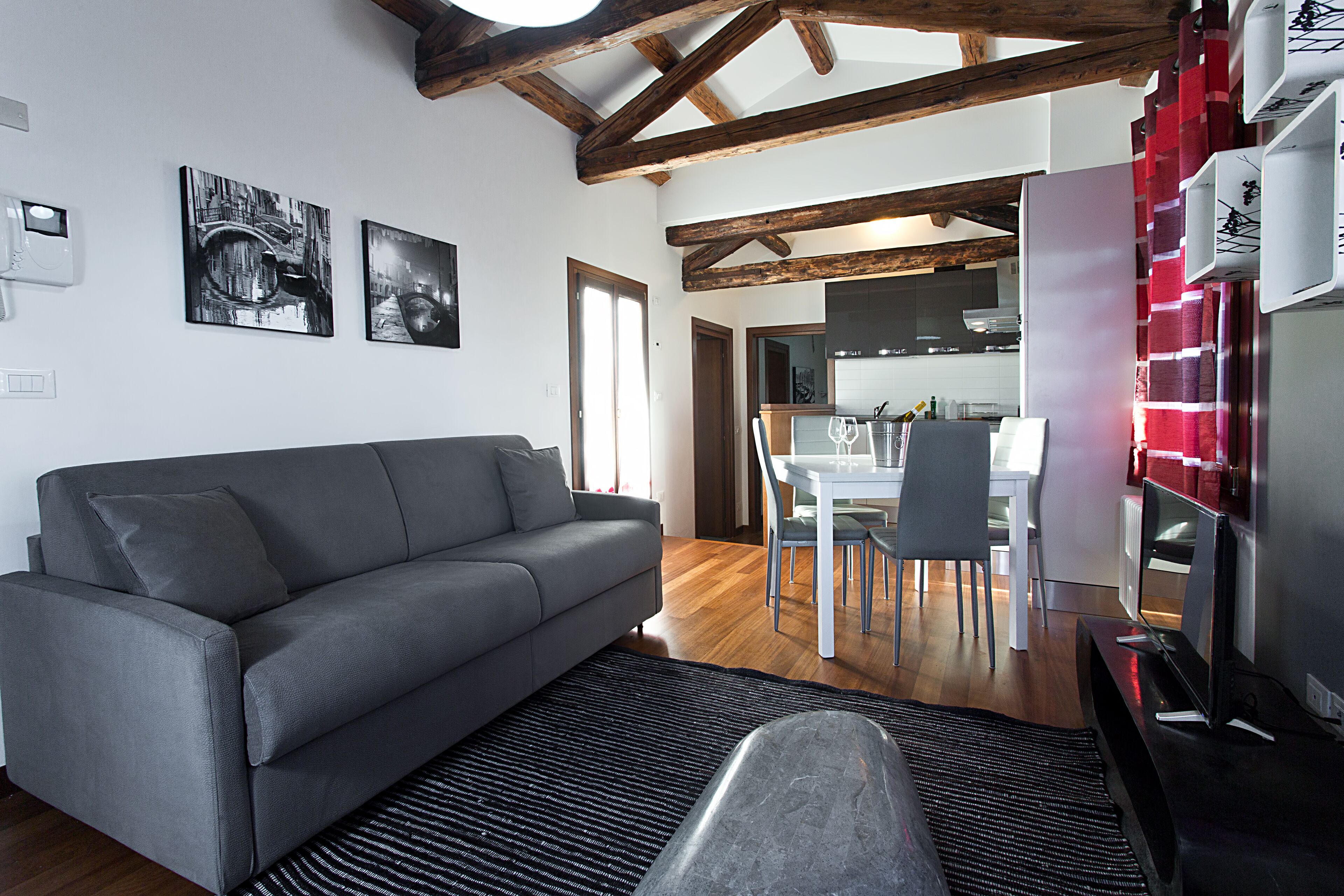 Een moderne woonkamer met een grijze bank, een zwart vloerkleed, en een eethoek met een witte tafel en stoelen.