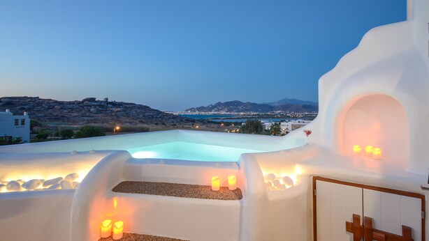 A rooftop pool with a view of a city and mountains at dusk.