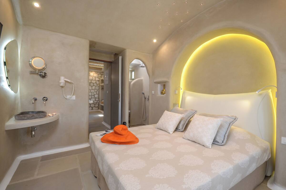 A modern bedroom with a bed, a bedside table, a built-in sink, and a shower area.