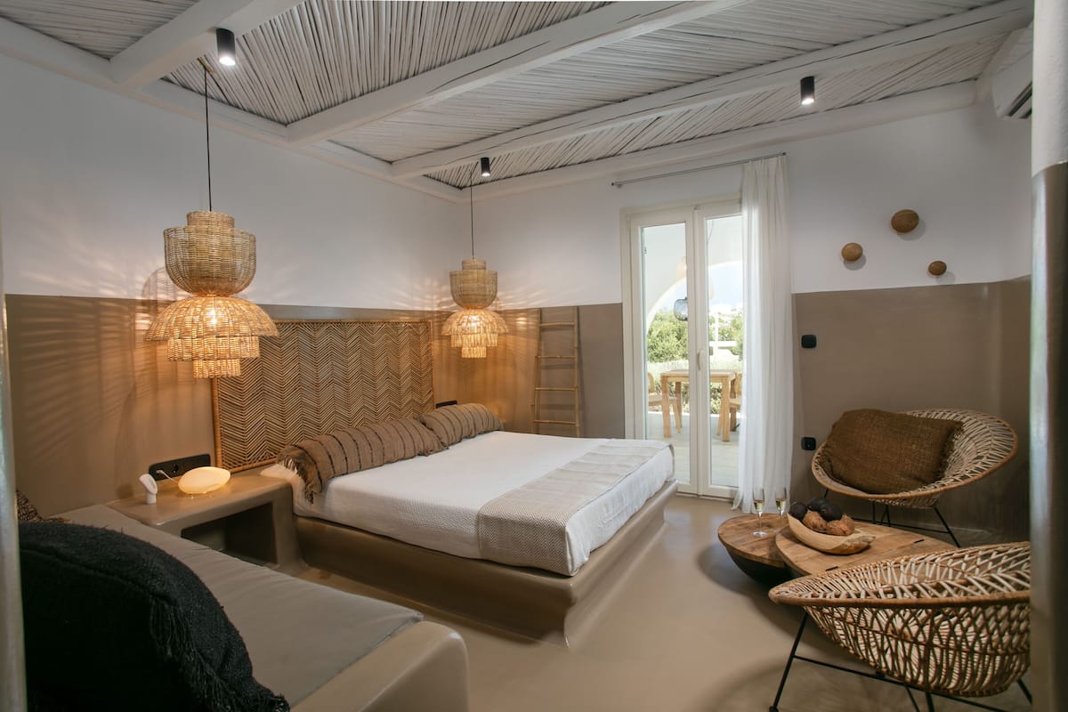 Un dormitorio moderno con una cama grande, dos lámparas colgantes, una silla de mimbre y vistas al exterior.