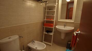 A bathroom with a toilet, bidet, sink, and shelves with towels.