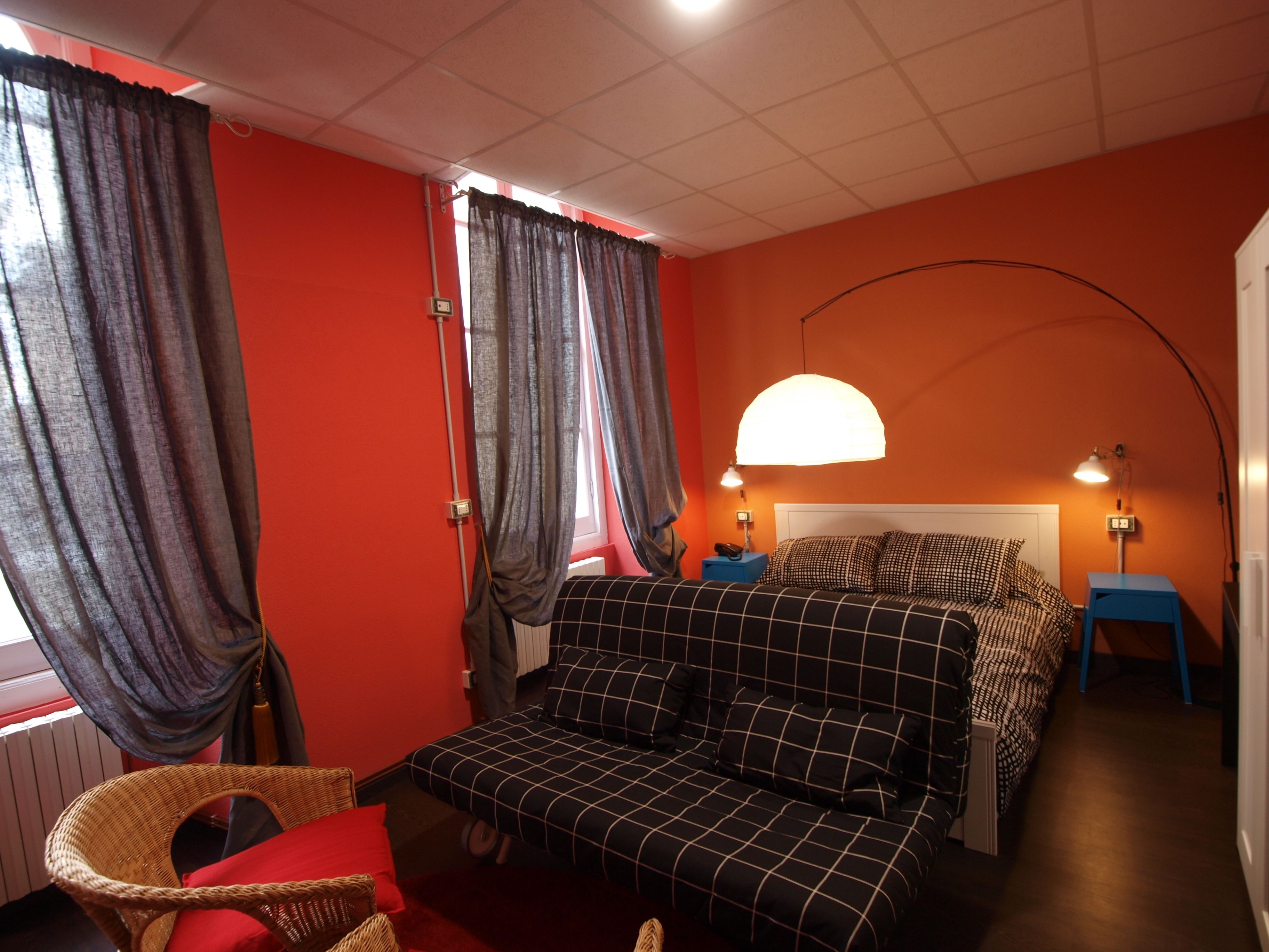 Ein Zimmer mit einem Bett, einem Sessel, einer Lampe und Vorhängen.