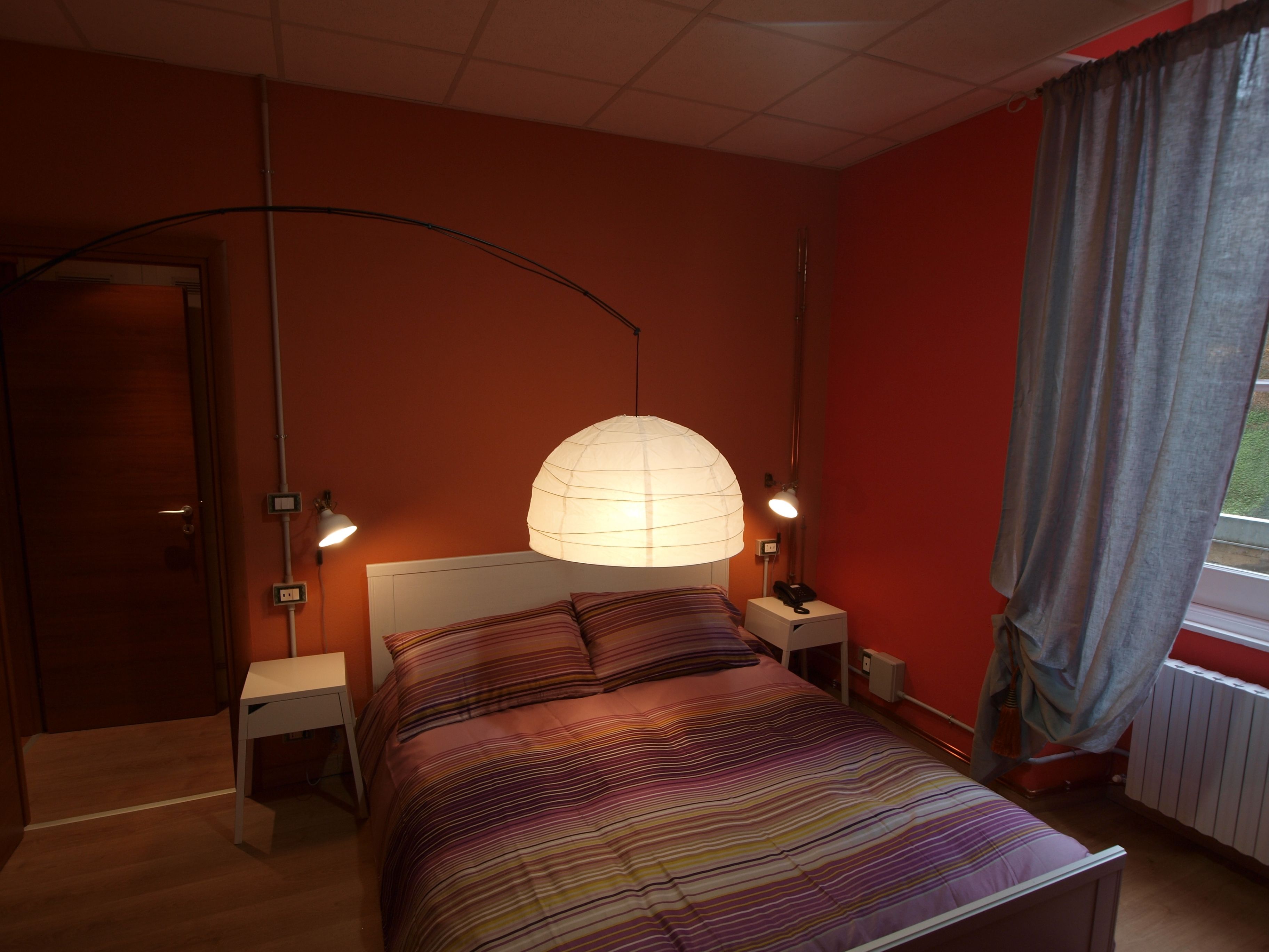 Una camera da letto con un letto, due comodini, una lampada e una finestra con tende.