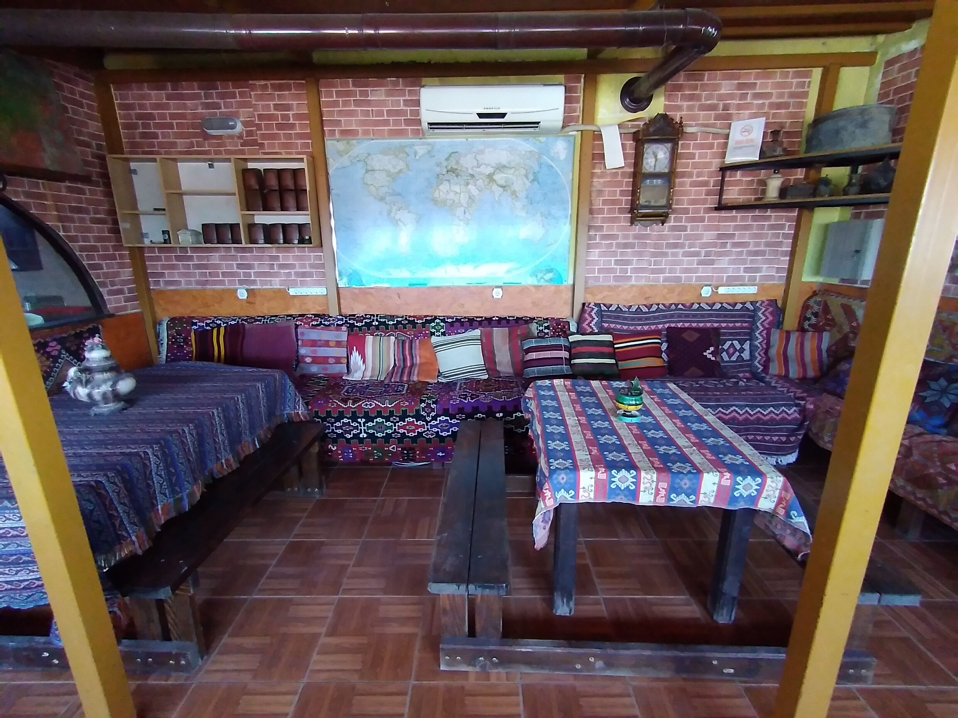 Una habitación rústica con pared de ladrillo, un mapa grande, un banco de madera y una mesa con manteles estampados.