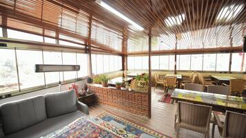 A spacious room with a large window, a sofa, a dining table with chairs, and a brick partition.
